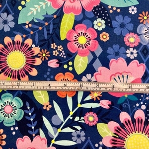 May include: A navy blue fabric with a colourful floral pattern. The fabric features pink, orange, yellow, green, and blue flowers. A ruler is placed on top of the fabric to show the scale.