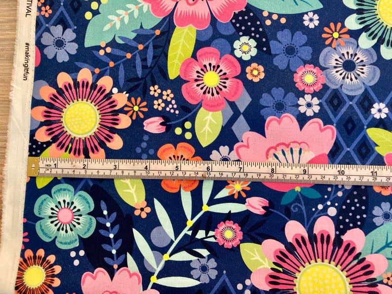 May include: A navy blue fabric with a colourful floral pattern. The fabric features pink, orange, yellow, green, and blue flowers. A ruler is placed on top of the fabric to show the scale.