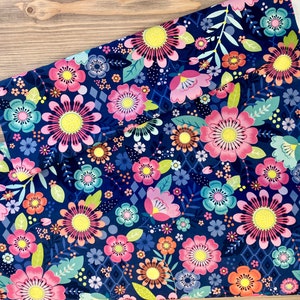 May include: A navy blue fabric with a floral print featuring pink, yellow, and blue flowers. The fabric has a repeating pattern of flowers and leaves.