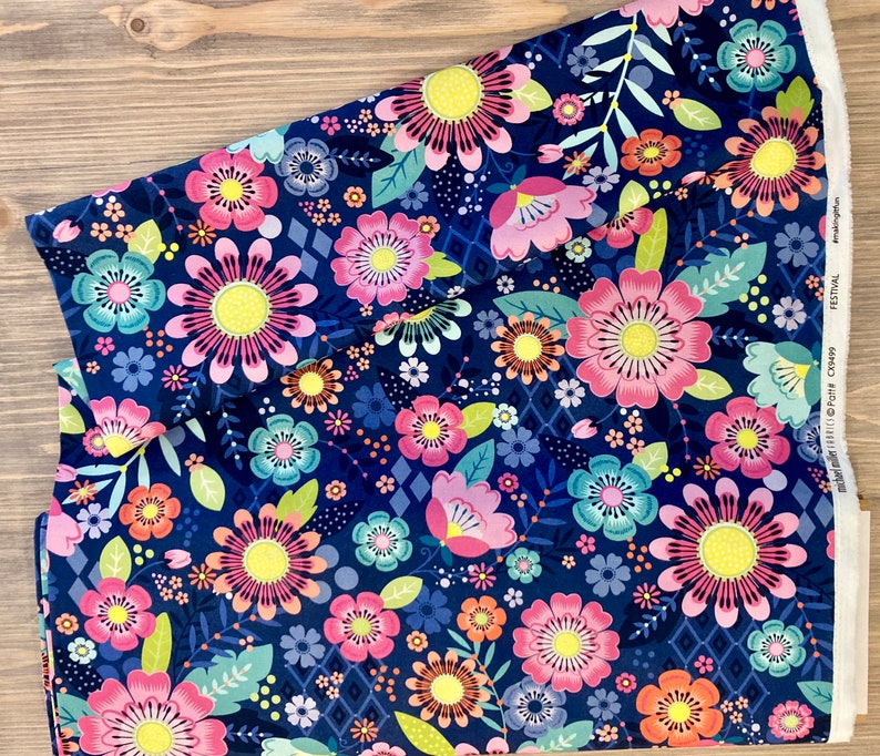 May include: A navy blue fabric with a floral print featuring pink, yellow, and blue flowers. The fabric has a repeating pattern of flowers and leaves.