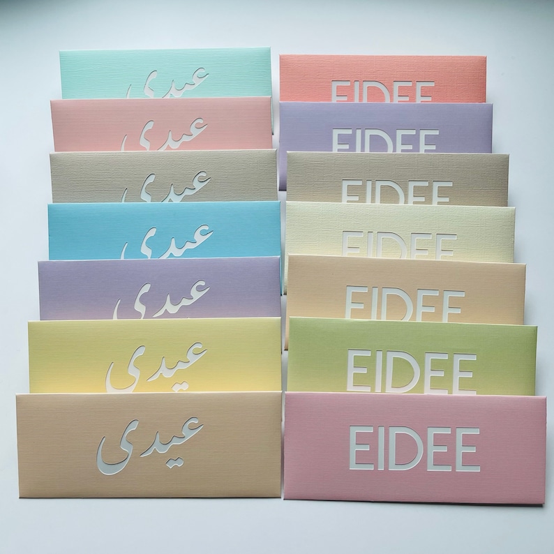 May include: A collection of pastel-colored rectangular envelopes. Each envelope features cut-out text, with some displaying the word "EIDEE" and others displaying Arabic script. The envelopes are arranged in neat rows, showcasing a variety of soft hues.