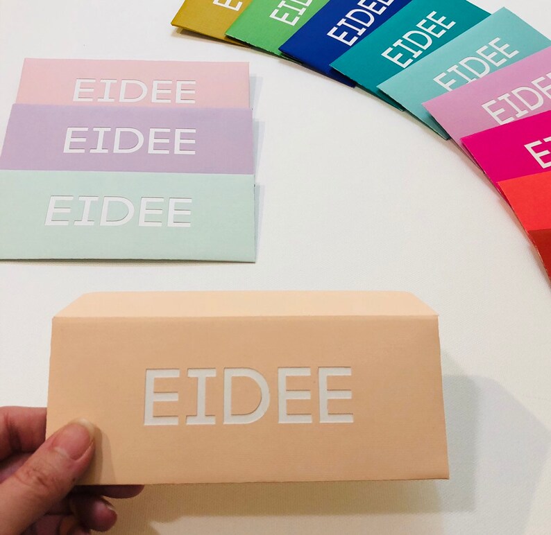 May include: A collection of pastel-colored envelopes with the word "EIDEE" embossed in white. The envelopes are in shades of pink, lavender, mint green, and peach. A hand holds a peach-colored envelope with the same text.