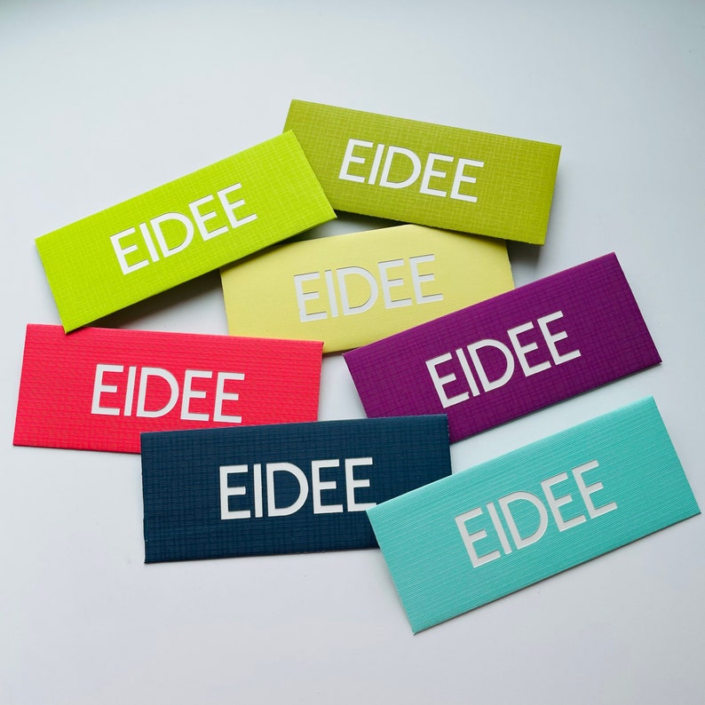 May include: A collection of rectangular cards in various colors, including green, red, purple, and blue. Each card features the word "EIDEE" in white, centered on the front. The cards have a textured surface.