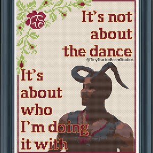 Op de afbeelding: Ingelijste kruissteekkunst met de tekst "It's not about the dance, it's about who I'm doing it with." De afbeelding toont een figuur met hoorns en bloemaccenten. De lijst is zwart.