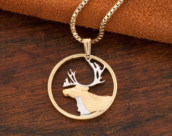 May include: Gold-tone pendant necklace featuring a detailed elk design. The elk is depicted in gold and silver tones within a circular frame, suspended from a delicate chain. The pendant is set against a dark wooden surface.