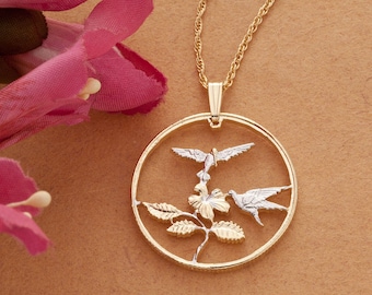 May include: Gold necklace with a round pendant featuring two hummingbirds in flight, a hibiscus flower, and leaves. The pendant is made of two-toned metal, with gold and silver accents.