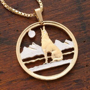 May include: A gold necklace with a round pendant featuring a wolf howling at the moon in a mountainous landscape. The pendant is made of gold and silver.