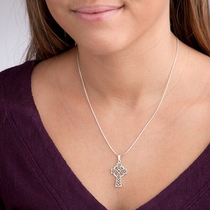 Peut inclure: Un collier avec un pendentif en forme de croix celtique argent&eacute;e. Le pendentif pr&eacute;sente un motif ajour&eacute; complexe. Le collier est pr&eacute;sent&eacute; sur un haut violet fonc&eacute;.