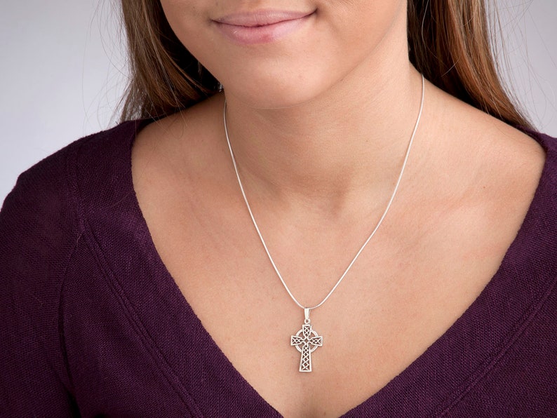 Peut inclure: Un collier avec un pendentif en forme de croix celtique argent&eacute;e. Le pendentif pr&eacute;sente un motif ajour&eacute; complexe. Le collier est pr&eacute;sent&eacute; sur un haut violet fonc&eacute;.