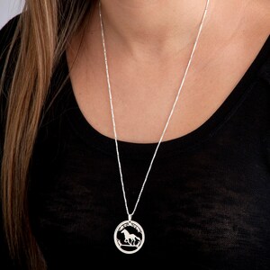 May include: A silver chain necklace with a round pendant featuring a cutout design of a horse running through a field.