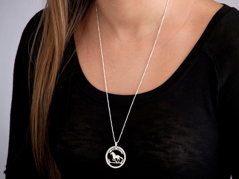 May include: A silver chain necklace with a round pendant featuring a cutout design of a horse running through a field.