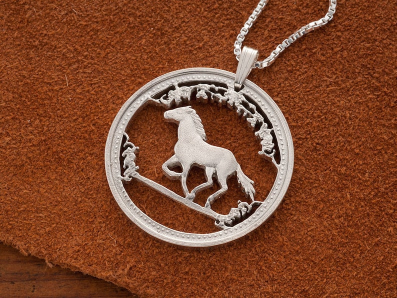 May include: Silver pendant necklace featuring a cutout design of a horse running through a field of flowers. The pendant is round and has a detailed design.