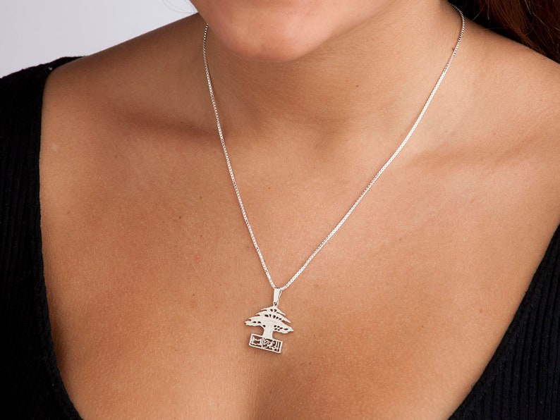 May include: A silver necklace with a pendant shaped like a cedar tree with the word "Lebanon" written on a banner below the tree.