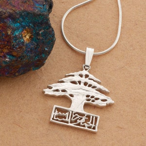May include: Silver necklace with a pendant shaped like a cedar tree, the national symbol of Lebanon. The pendant is detailed with a stylized tree trunk and branches, and the base features a design of three horizontal lines.