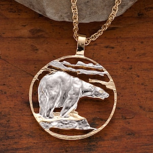 May include: A gold necklace with a round pendant featuring a detailed silver polar bear standing on a rocky surface. The pendant is cut out to show the bear's outline.
