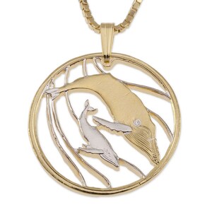 May include: Gold and silver tone pendant necklace featuring a mother whale and calf. The whales are depicted in a stylized design with a textured surface. The pendant is round and hangs from a gold chain.