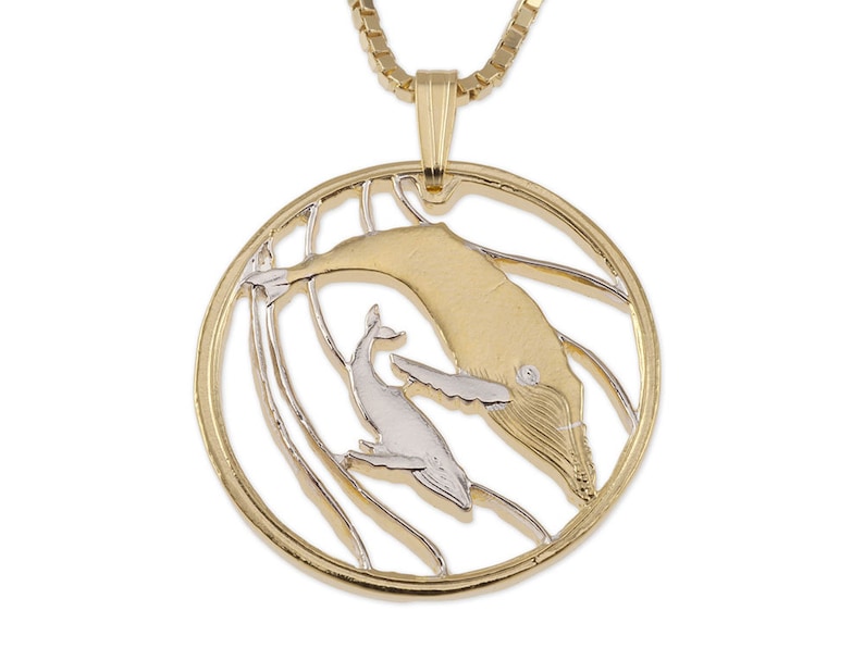 May include: Gold and silver tone pendant necklace featuring a mother whale and calf. The whales are depicted in a stylized design with a textured surface. The pendant is round and hangs from a gold chain.