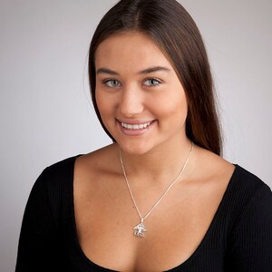 May include: A woman with long brown hair is wearing a black shirt and a silver necklace with a tree pendant. The pendant has the word "love" inscribed on it.