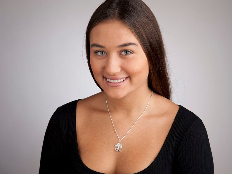 May include: A woman with long brown hair is wearing a black shirt and a silver necklace with a tree pendant. The pendant has the word "love" inscribed on it.