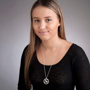 May include: A woman wearing a black shirt with a silver necklace featuring a circular pendant with a horse silhouette.