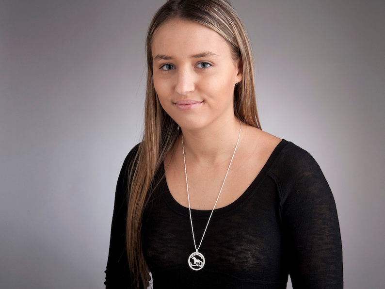 May include: A woman wearing a black shirt with a silver necklace featuring a circular pendant with a horse silhouette.