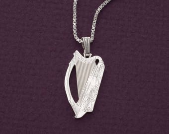 May include: A silver-colored pendant necklace featuring a detailed harp design. The harp pendant is suspended from a delicate chain. The background is a solid, dark purple color.