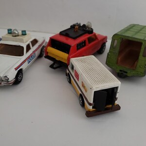 May include: A collection of vintage toy cars, including a white police car, a red station wagon, a green van, and a white delivery truck. The cars are all in good condition and have a classic look.