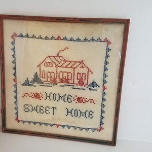 May include: A framed cross-stitch embroidery with a red house and the text "Home Sweet Home" in blue and red thread.