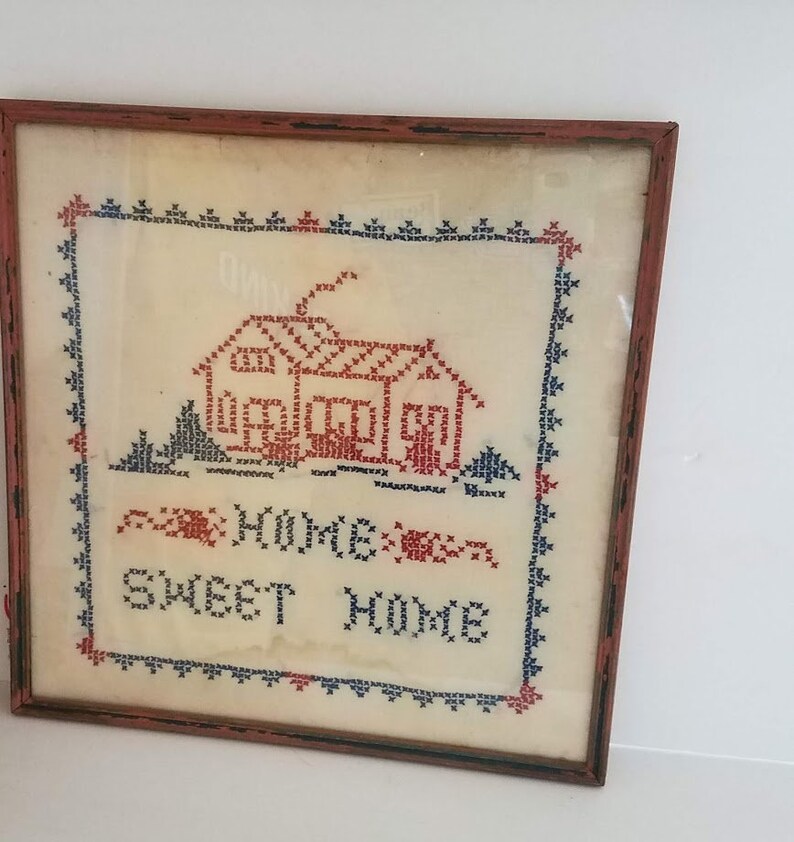 May include: A framed cross-stitch embroidery with a red house and the text "Home Sweet Home" in blue and red thread.