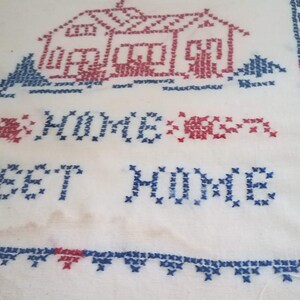 May include: Framed cross-stitch embroidery with a red and blue house and the text "Sweet Home" in blue thread.
