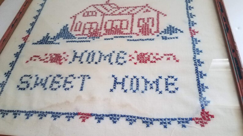May include: Framed cross-stitch embroidery with a red and blue house and the text "Sweet Home" in blue thread.
