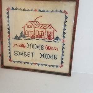 May include: A framed cross-stitch embroidery with a red house and the text "Home Sweet Home" in blue and red thread.