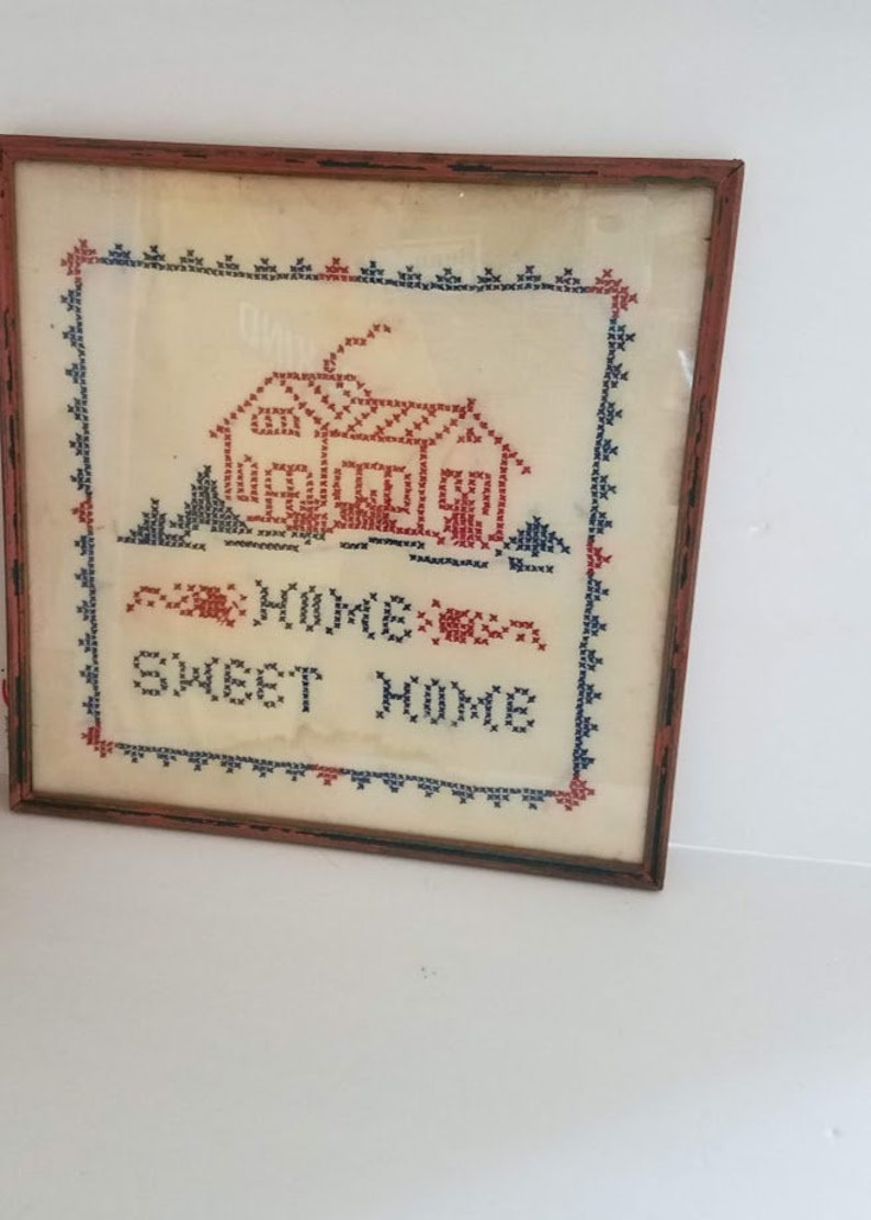 May include: A framed cross-stitch embroidery with a red house and the text "Home Sweet Home" in blue and red thread.