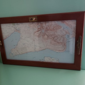 May include: A wooden framed map tray with a nautical map of a coastline and a small flag on the top right corner.