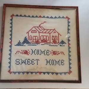 May include: A framed cross-stitch with a red and blue house design and the words "Home Sweet Home".
