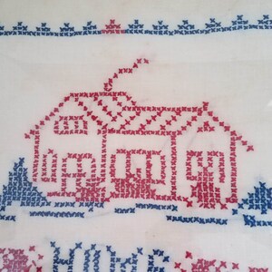 May include: A framed cross-stitch embroidery depicting a red house with a blue chimney and two blue trees. The text "Home Sweet Home" is stitched below the house.