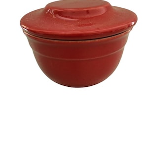 May include: A red ceramic butter dish with a lid. The dish has a rounded shape and a smooth, glossy finish.