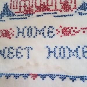 May include: White fabric with blue and red cross-stitch embroidery. The embroidery reads "Home Sweet Home".