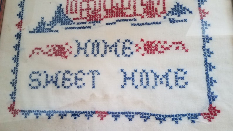 May include: White fabric with blue and red cross-stitch embroidery. The embroidery reads "Home Sweet Home".