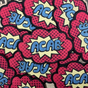 Op de afbeelding: Meerdere rode, gele en blauwe geborduurde patches met de tekst "ACAB" in een stripboek stijl.