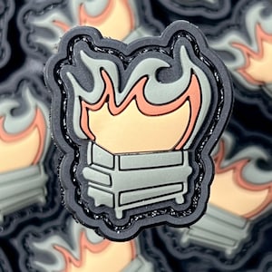 May include: A patch featuring a stylized campfire design. The patch has a black border with a gray and orange flame design over a gray rectangular base. The patch is likely made of rubber or a similar material.