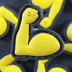 May include: A yellow rubber charm shaped like a bicep flexing with a black outline.
