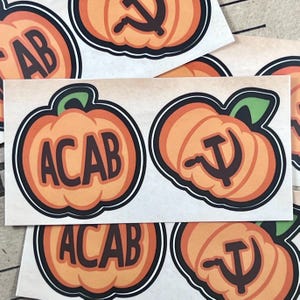 Könnte beinhalten: Vier orangefarbene Kürbisaufkleber mit schwarzen Umrissen. Zwei Aufkleber zeigen das Akronym "ACAB" und zwei Aufkleber zeigen Hammer und Sichel.