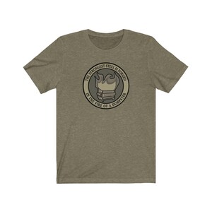 Pode incluir: Uma camiseta verde com um design gráfico circular. O gráfico apresenta um caixote do lixo em chamas com o texto "The strongest steel is forged in the fire of a dumpster".