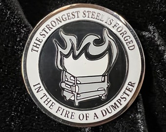 May include: A silver-colored round pin with a black and white image of a dumpster on fire. The text "The strongest steel is forged in the fire of a dumpster" is written around the image.