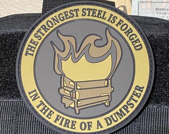 Może przedstawiać: Okrągła naszywka w kolorze czarnym i złotym z tekstem "The strongest steel is forged in the fire of a dumpster". Naszywka przedstawia stylizowany obraz kontenera na śmieci z płomieniami wychodzącymi z góry.