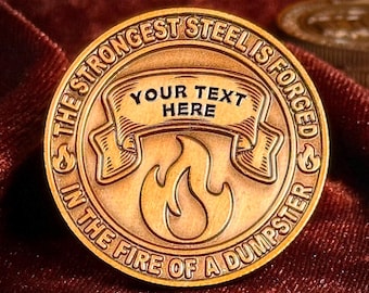 May include: A gold-colored metal coin with the text "& THE STRONGEST STEEL IS FORGED IN THE FIRE OF A DUMPSTER &" around the edge. In the center is a stylized flame with a banner above it that says "YOUR TEXT HERE".