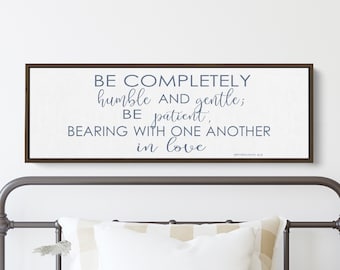 May include: A framed canvas print with a white background and brown frame. The text on the canvas reads "BE COMPLETELY humble AND gentle; BE patient, BEARING WITH ONE ANOTHER in love EPHESIANS 4:2".