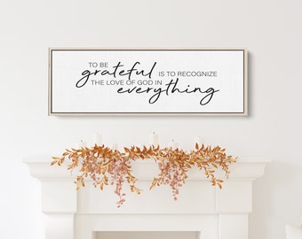 Pode incluir: Uma placa branca enquadrada com o texto "To be grateful is to recognize the love of God in everything" pendurada acima de uma lareira branca decorada com uma guirlanda de folhas de outono.