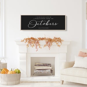 May include: A black and white sign with the quote "I'm so glad I live in a world where there are Octobers - Anne of Green Gables" hanging above a white fireplace mantel decorated with fall foliage.